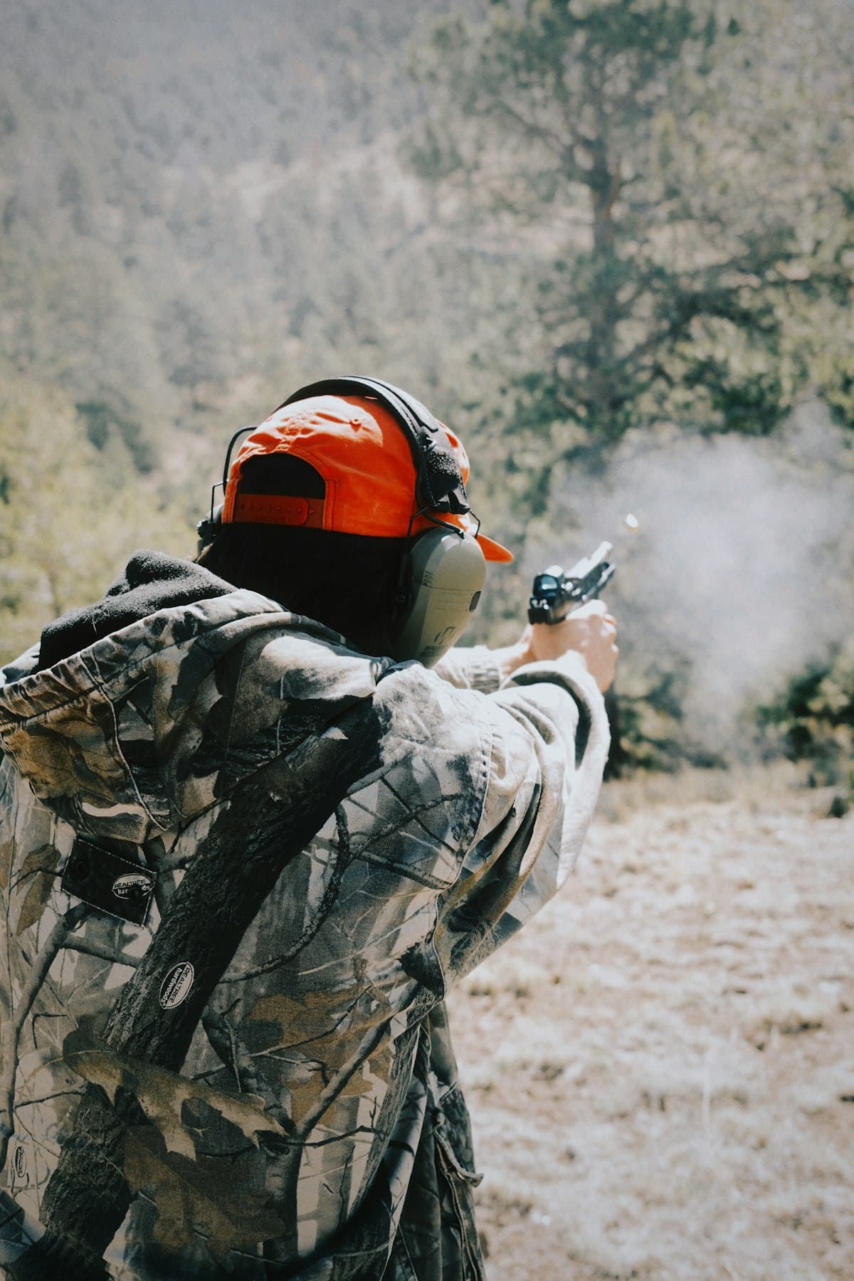 Shooter firing a pistol outdoors with visible muzzle flash